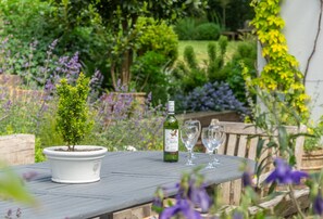 Un jardin, avec une plante en pot, une bouteille et deux verres posés sur une table en bois.