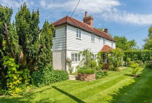 A two-story house with a red-tiled roof, surrounded by lush greenery and a well-maintained lawn.