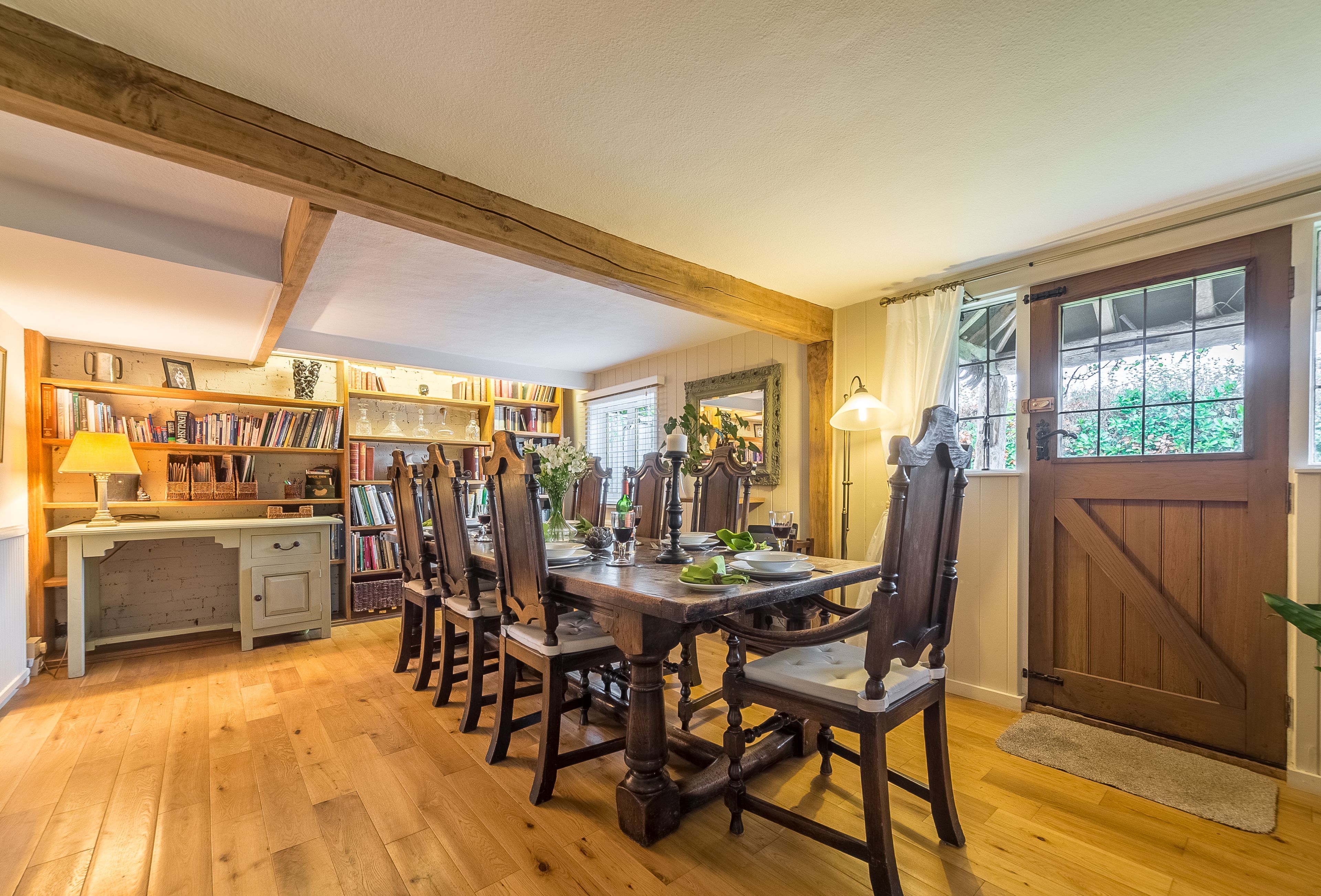 A dining area with a wooden table and chairs, a bookshelf, and a window with curtains.