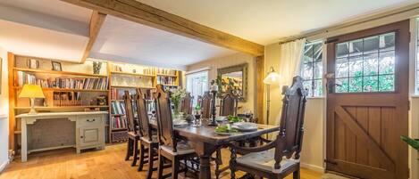 A dining area with a wooden table and chairs, a bookshelf, and a window with curtains.