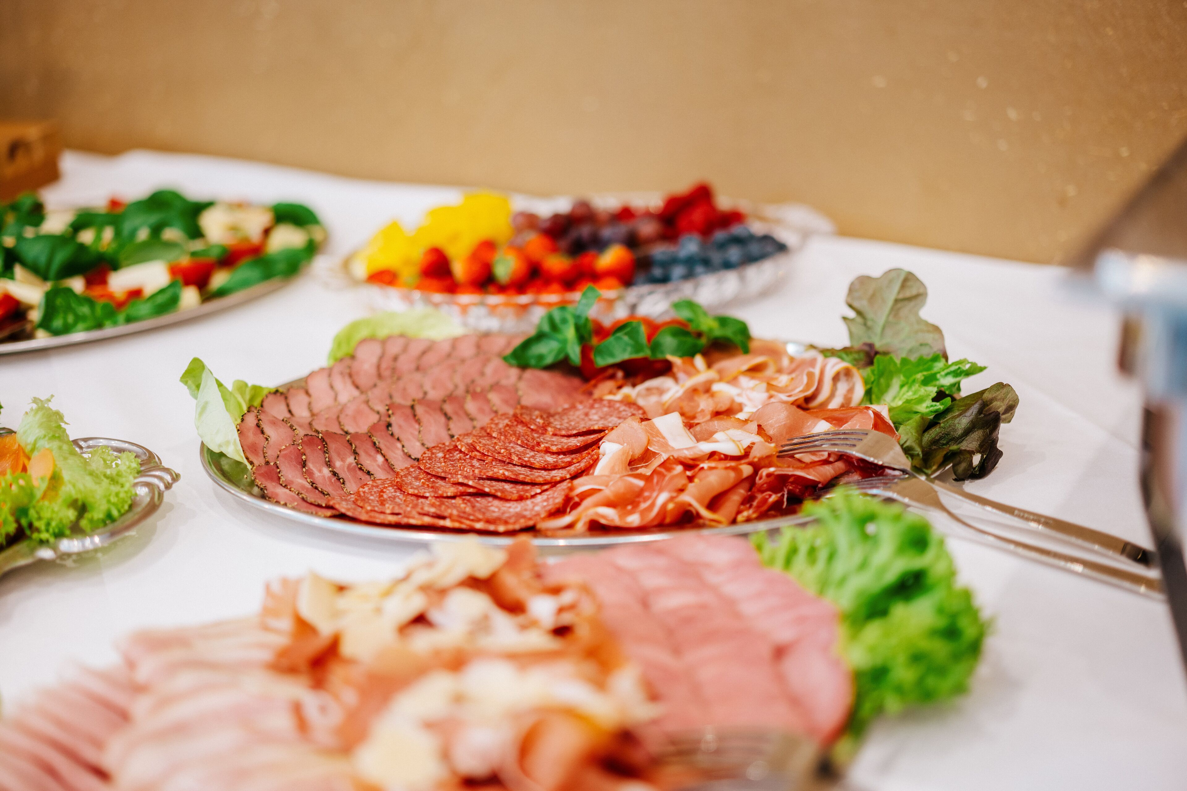 Variedad de alimentos sobre una mesa, incluyendo carnes en rodajas y verduras frescas.