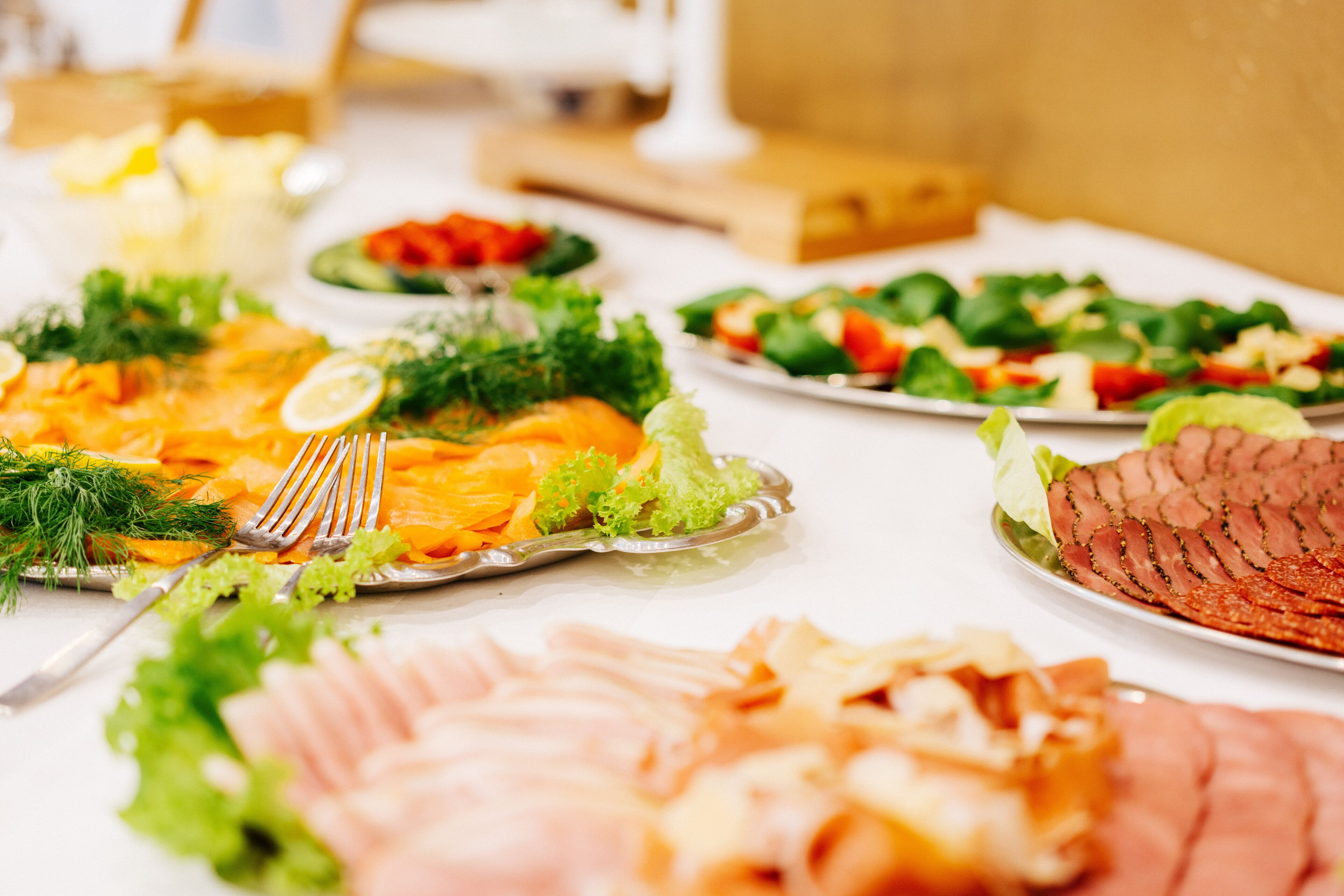 A buffet table with various dishes including sliced meats, salads, and garnishes.