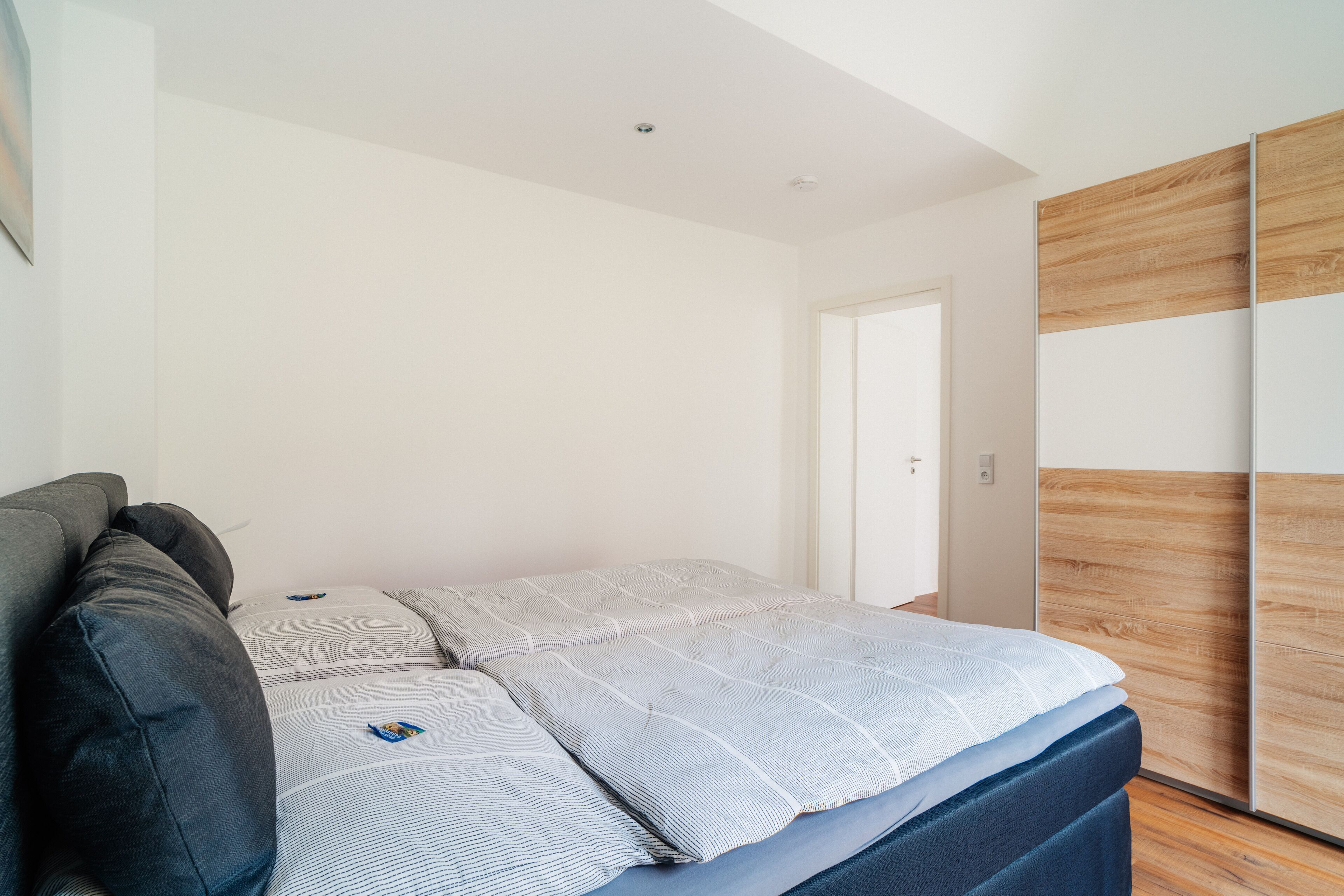 A modern bedroom with a bed, a dark sofa, and a wooden wardrobe.