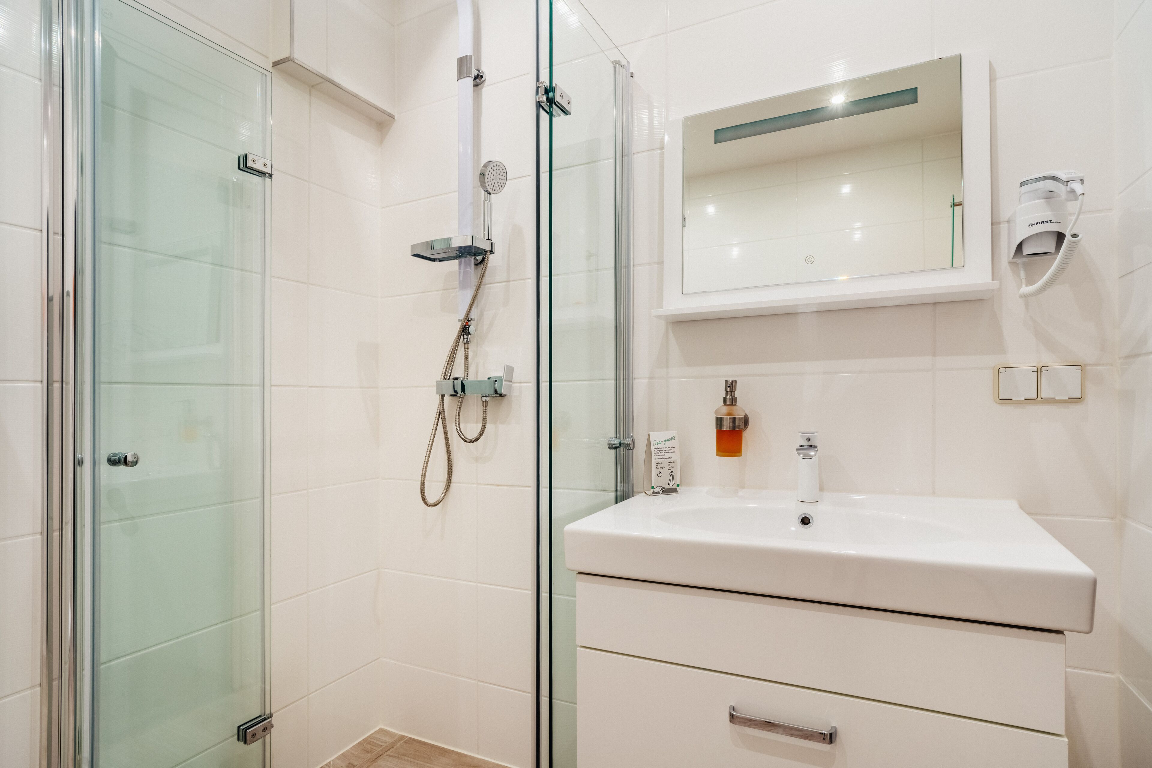 A modern bathroom with a glass-enclosed shower, a white sink, and a mirror above it.