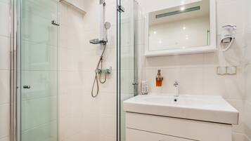 Een moderne badkamer met een douchecabine van glas, een witte wastafel en een spiegel erboven.
