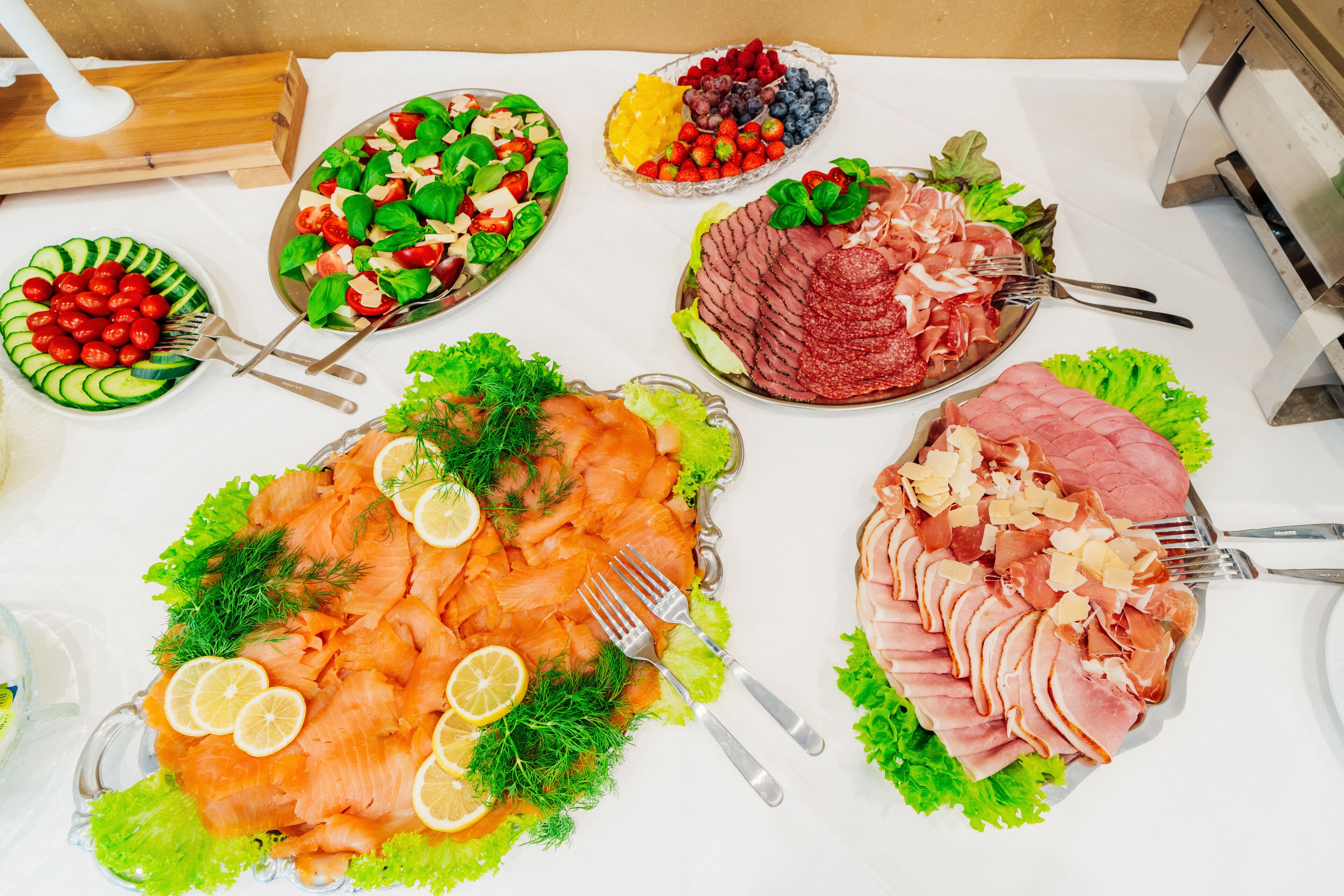 A table with various food platters including salmon, ham, and fresh fruits.