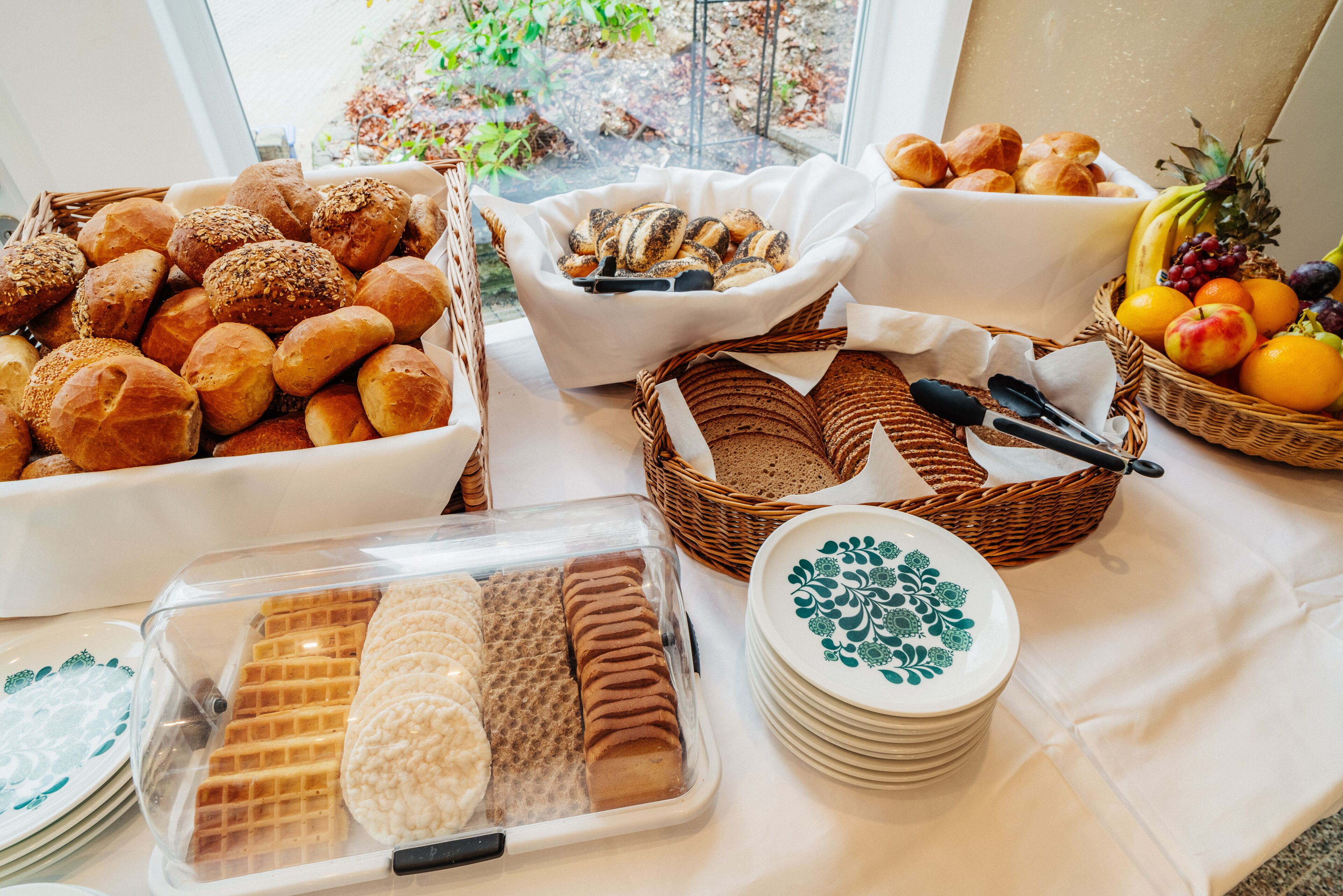 Un buffet proposant une variété de produits de boulangerie, notamment du pain et des viennoiseries, ainsi qu’un assortiment de fruits et de légumes.