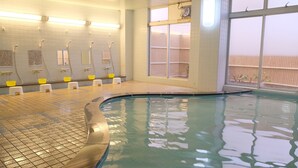 An indoor swimming pool with tiled walls, multiple showerheads, and a large window with a view of a wooden fence. - Sunset Susami (Susami)