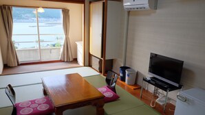 A room with tatami mats, a wooden table, a television, a refrigerator, and a view of a body of water. - Sunset Susami (Susami)