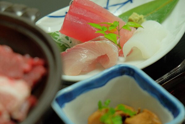 A plate with various types of sashimi, including pink and white fish, garnished with a small green leaf.