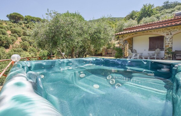 Un jacuzzi en un jardín con una casa de piedra y árboles al fondo.