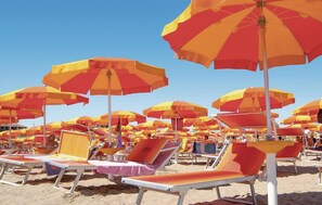 Una playa con numerosos sombrillas y tumbonas.
