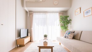 Una sala de estar moderna con un sofá, una mesa de centro, un televisor y un amplio ventanal con cortinas.