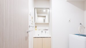 Un baño con lavamanos blanco, espejo y toallero.
