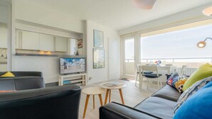 Una sala de estar moderna con un sofá de cuero negro, una mesita blanca y un televisor.