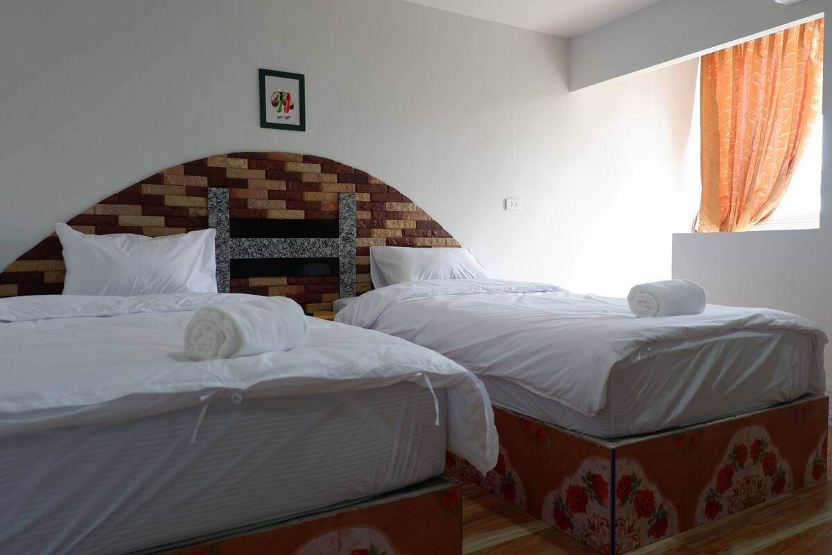 Two beds with white linens, a brick-patterned headboard, and a small framed picture on the wall.