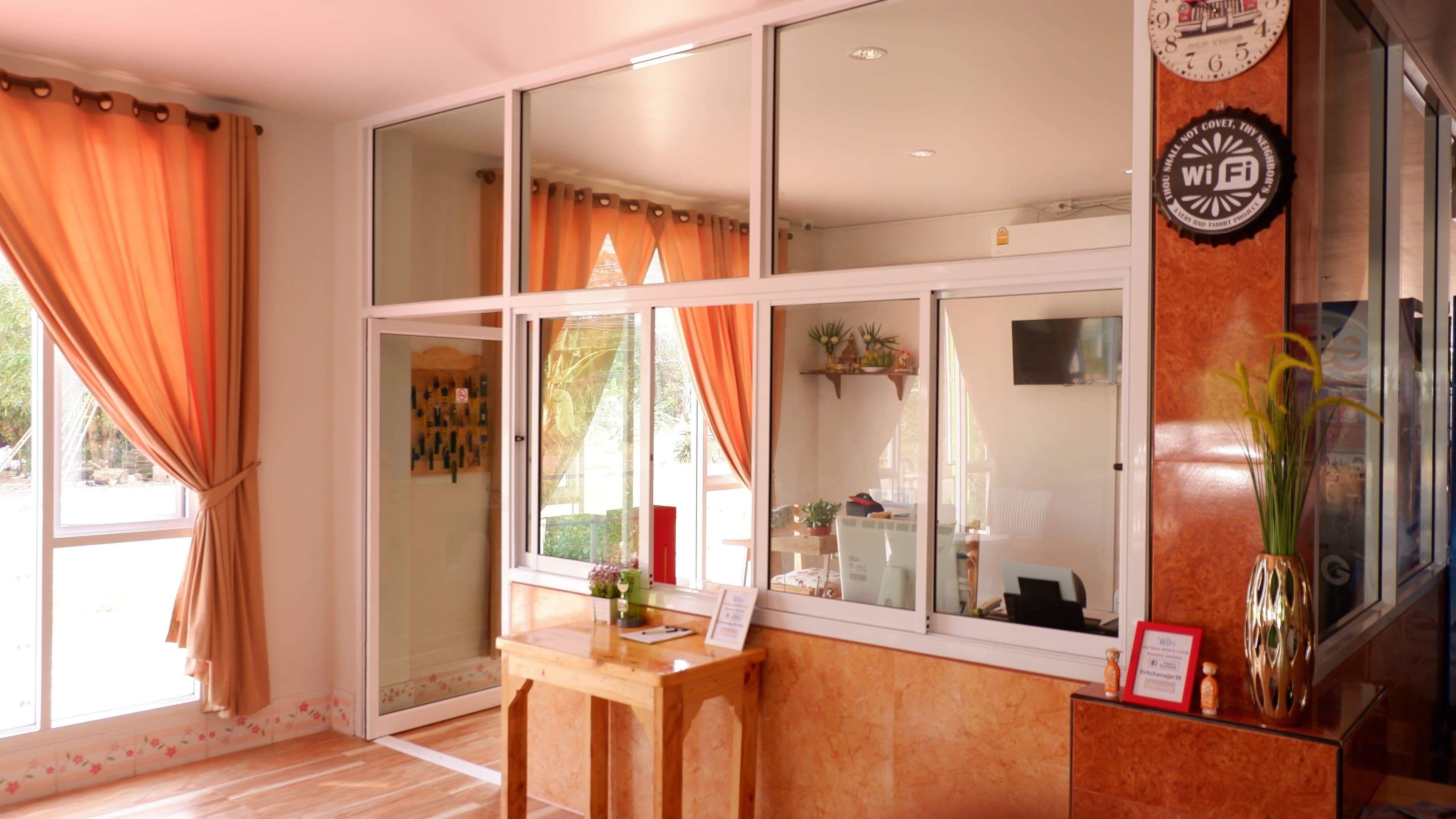 A room with large windows, a wooden desk, and a reception area with a vase and a clock.