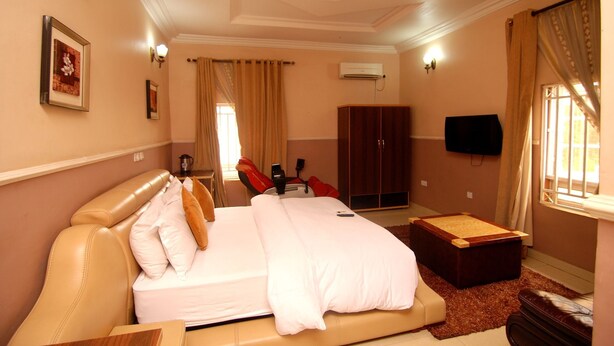 Ein Hotelzimmer mit einem großen Bett, einer Holzkommode, einem Schreibtisch und einem an der Wand befestigten Fernseher.