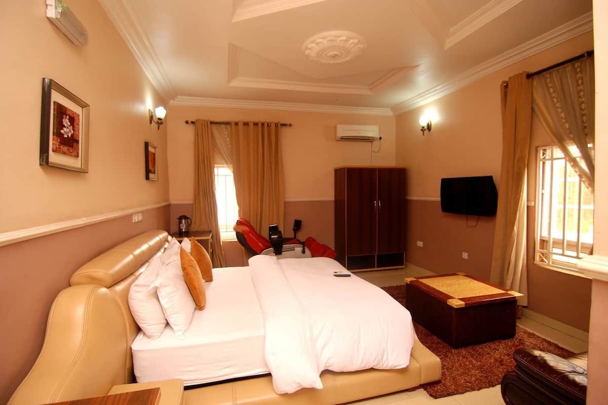 A hotel room with a large bed, a wooden chest of drawers, a desk, and a television on the wall.