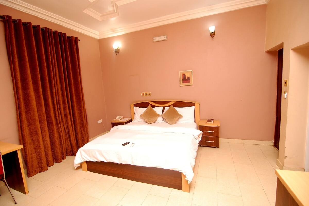 A bedroom with a large bed, a wooden nightstand, a desk, and a red curtain.