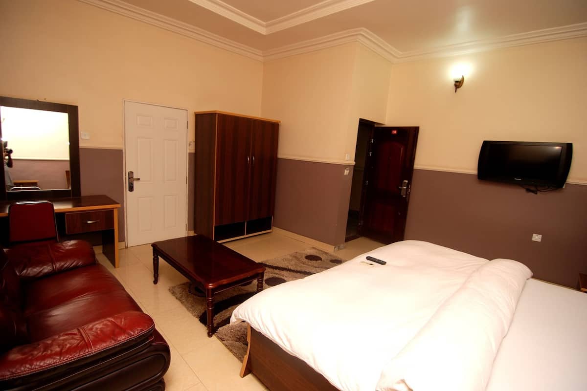 A hotel room with a bed, a desk, a chair, a wardrobe, and a television.