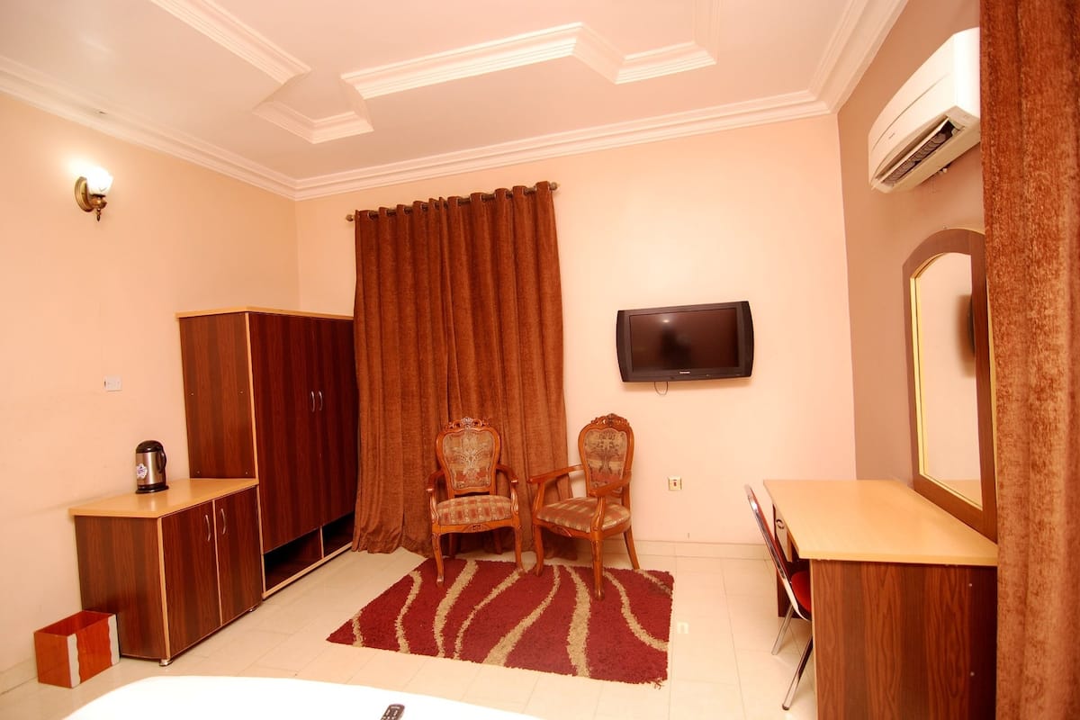 A hotel room with a wooden wardrobe, two chairs, a TV mounted on the wall, and a mirror.