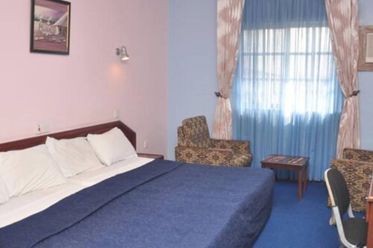 A hotel room with a bed, two chairs, a small table, and a window with curtains.