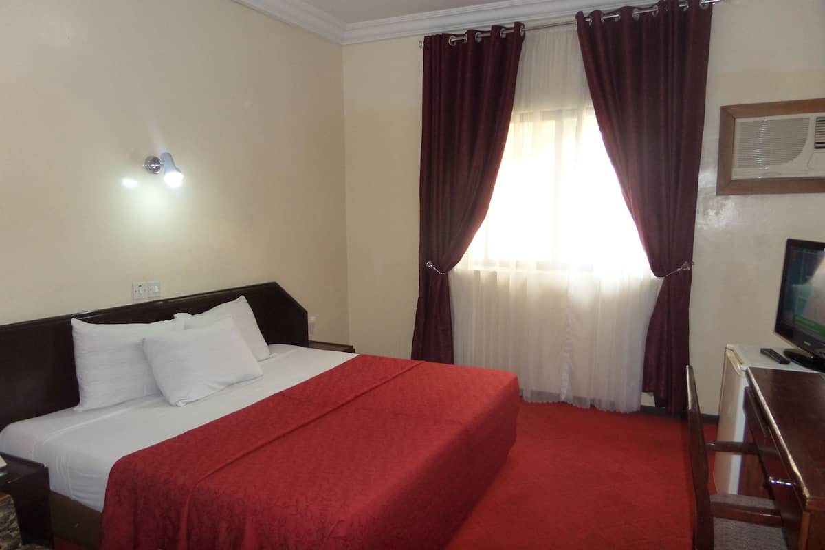 A hotel room with a bed, a desk, a chair, a television, and a window with curtains.