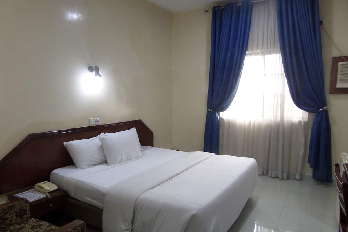 A hotel room with a bed, a nightstand, a telephone, and a chair.