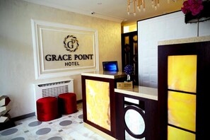 A reception area with a sign reading "GRACE POINT HOTEL," a reception desk, a computer monitor, and red ottomans. - Grace Point Resort Hotel (Abuja)