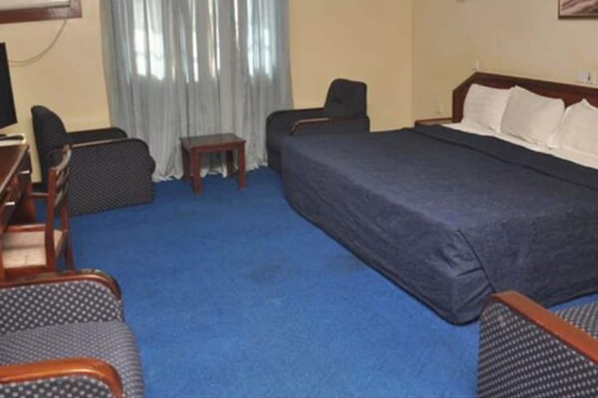 A hotel room with a large bed, two armchairs, a small table, and a TV.