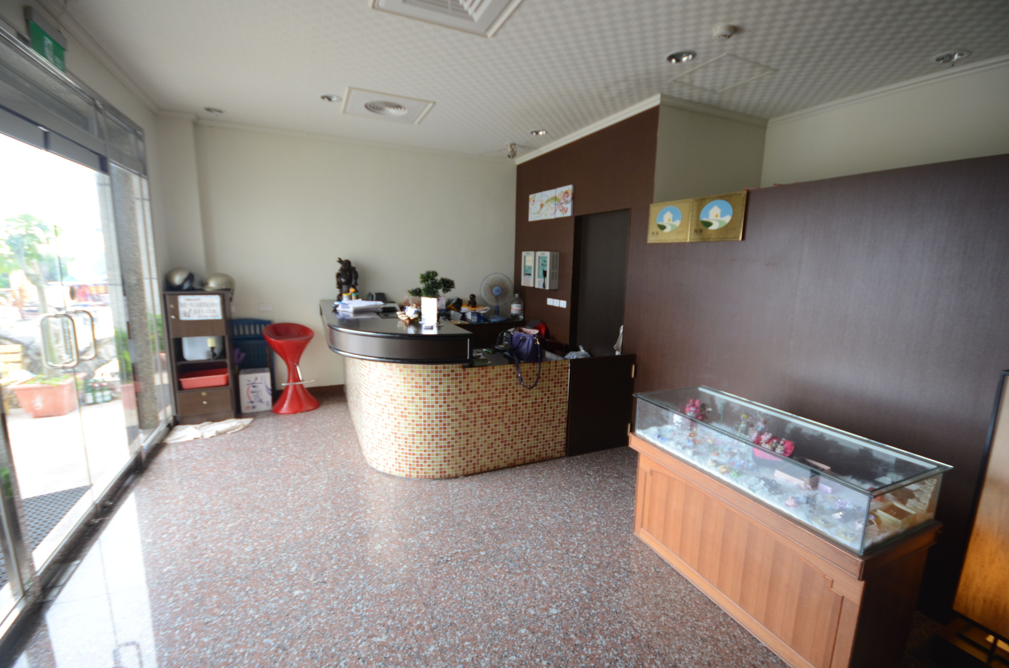 Un espace d’accueil comprenant un comptoir, une vitrine et un coin salon avec un fauteuil rouge.