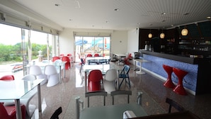 Een modern restaurant met een bar, glazen tafels en rode en witte stoelen.