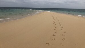 Een zandstrand met voetaal die naar het water leidt, onder een bewolkte lucht.