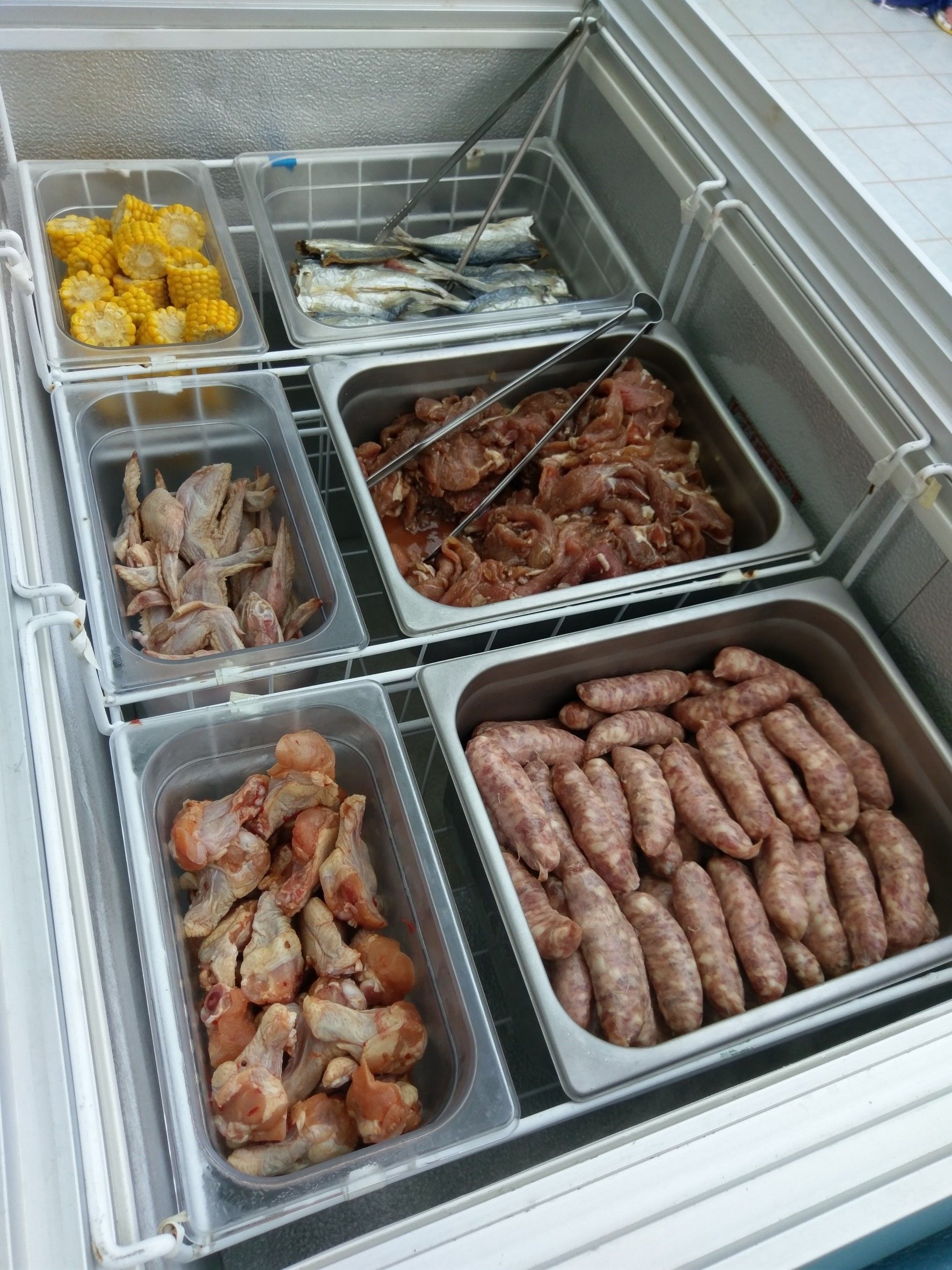 En buffé med ett varierat utbud av mat, inklusive majs, fisk, kyckling och korv.