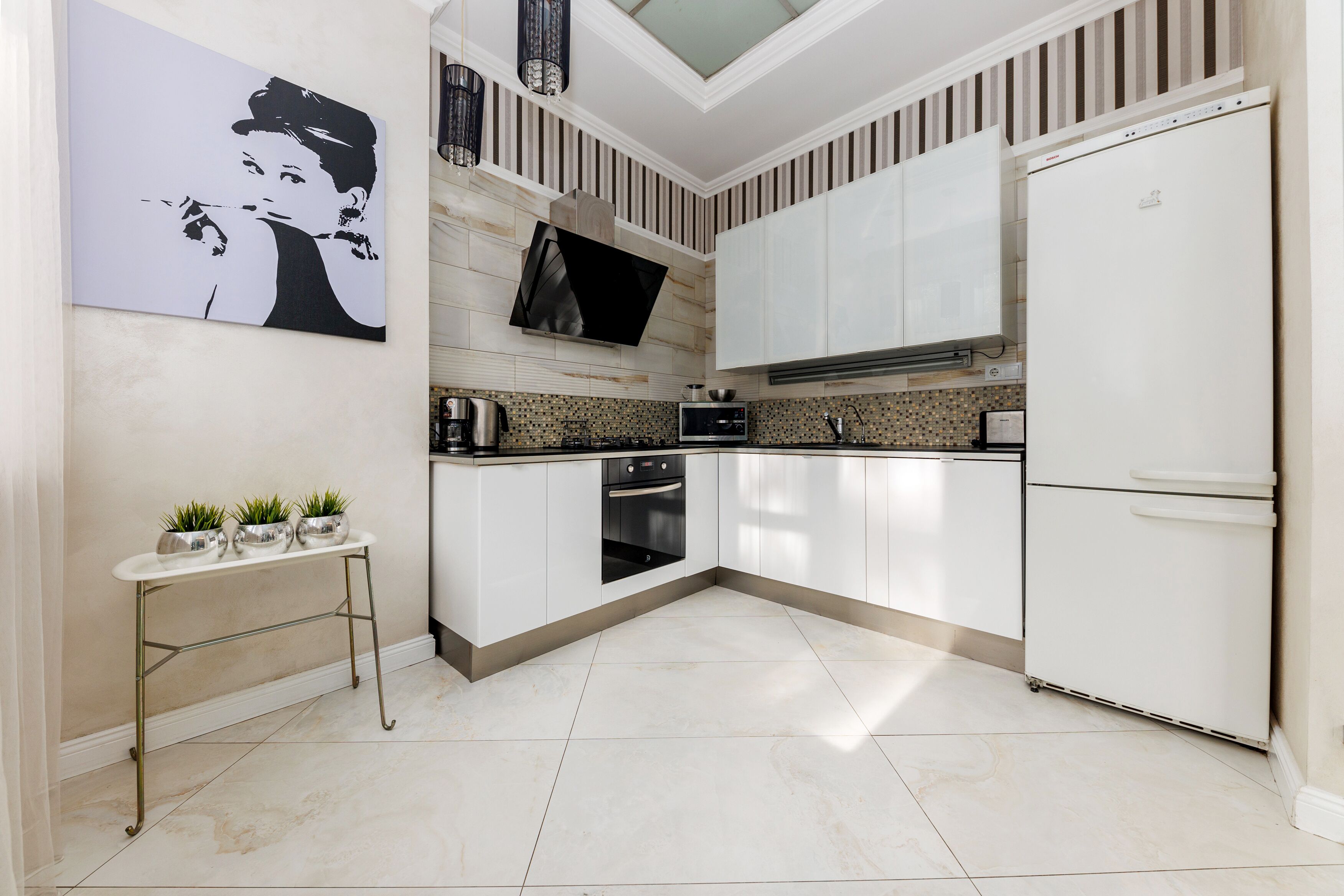 Una cocina moderna con armarios blancos, horno empotrado, microondas y refrigerador blanco.