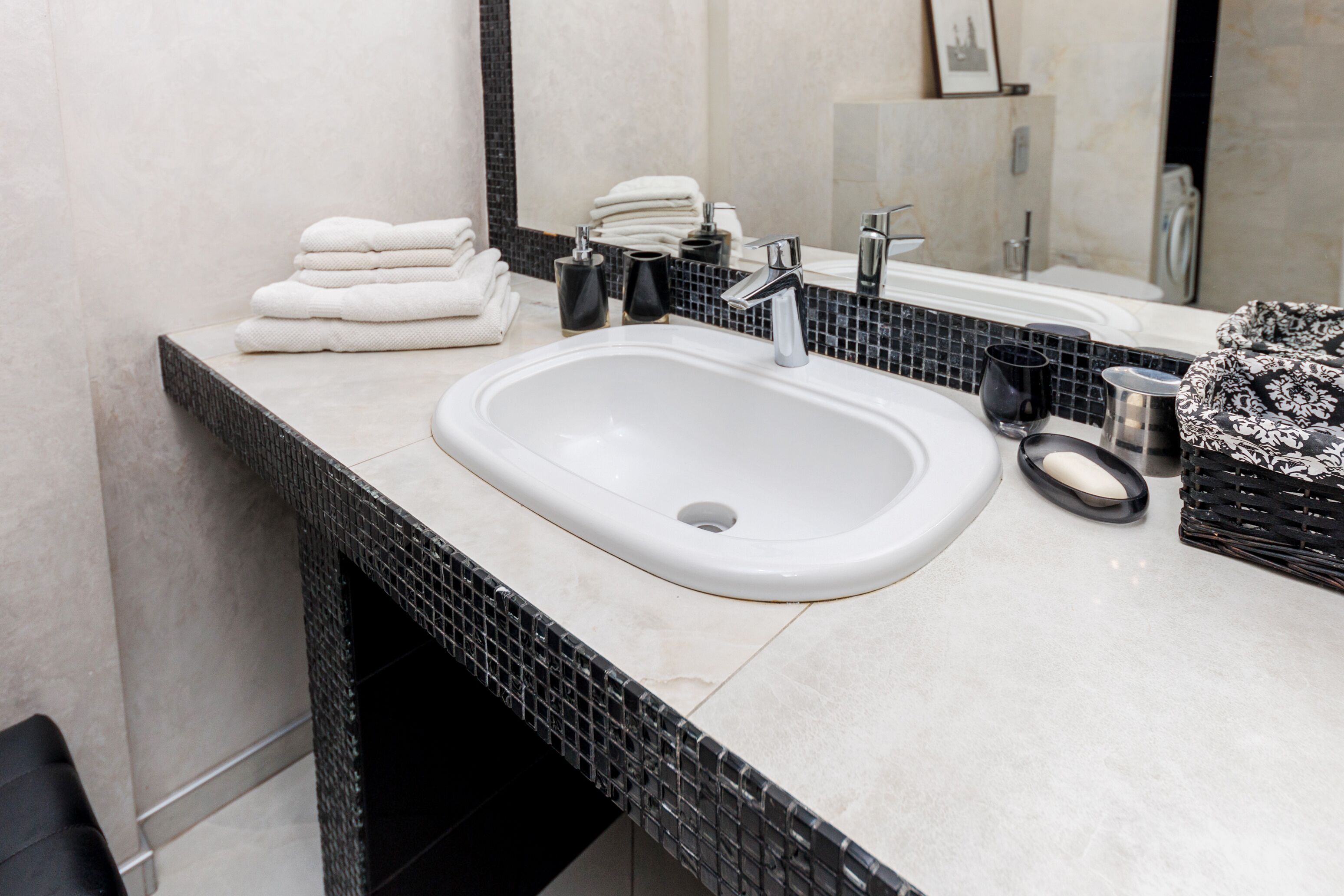 Une salle de bain avec un lavabo blanc, un pare-feu en carreaux noirs et blancs, un miroir et une pile de serviettes blanches.