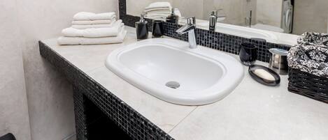 Une salle de bain avec un lavabo blanc, un pare-feu en carreaux noirs et blancs, un miroir et une pile de serviettes blanches.