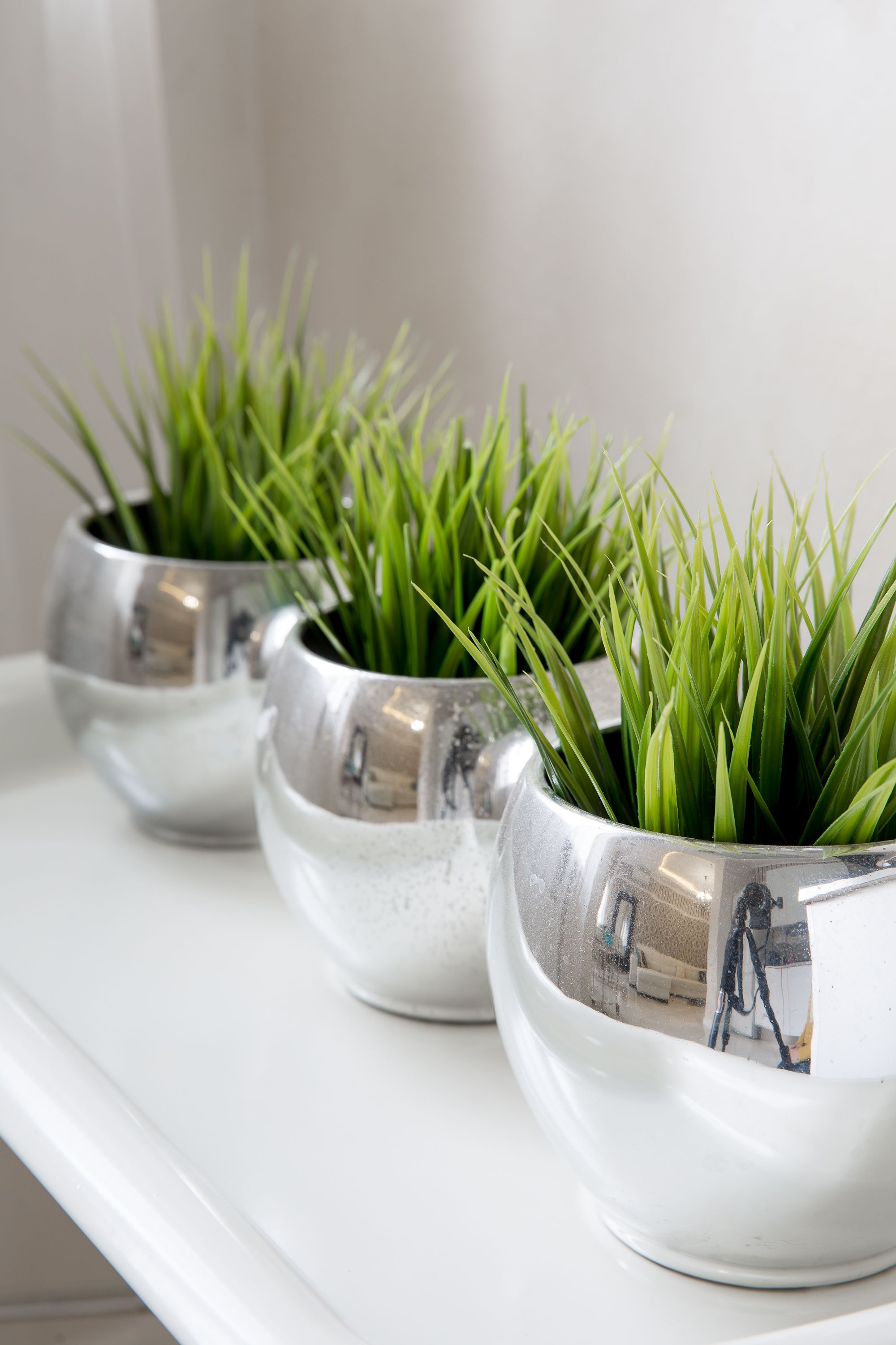 Three metallic planters with green plants on a white shelf.
