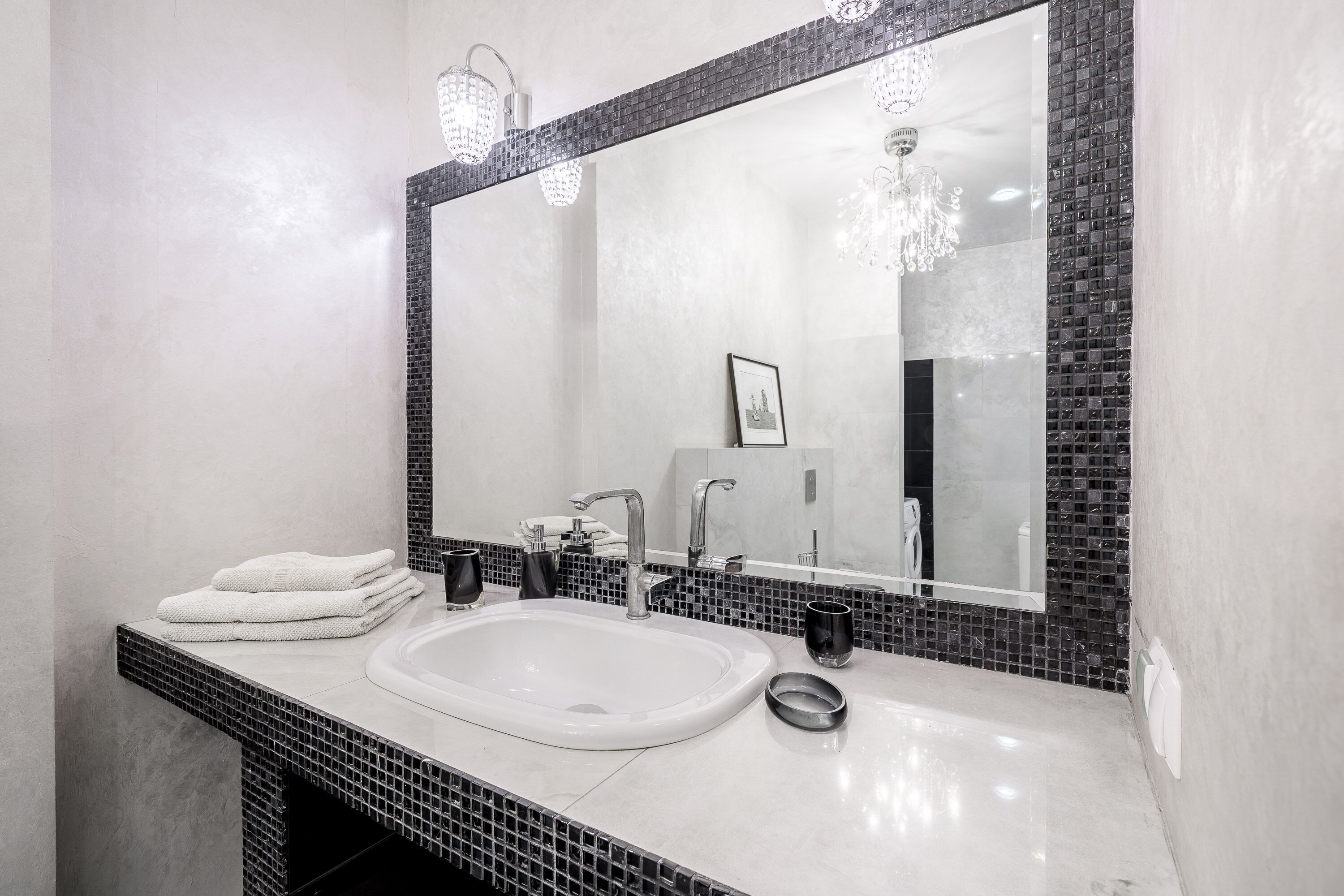 A bathroom with a large mirror, a sink, and a towel stack.