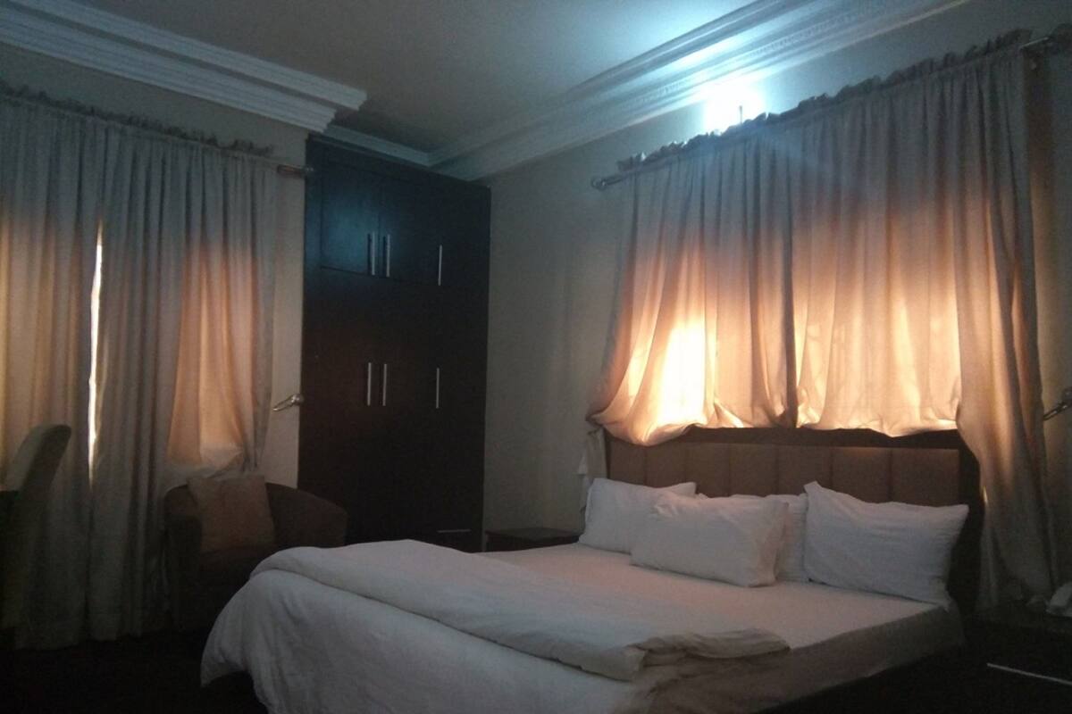A hotel room with a large bed, a wardrobe, and curtains.
