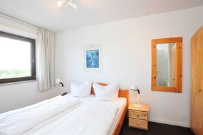 Quarto de hotel com cama, mesa de cabeceira, luminária e um espelho grande.