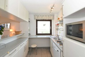 Cozinha compacta com armários brancos, micro-ondas, pia e janela com cortina.