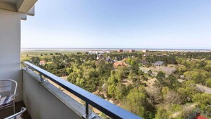 A balcony with a view of a residential area, a body of water, and a distant shoreline. - Apartment 187 (ID 093) (Sankt Peter-Ording)