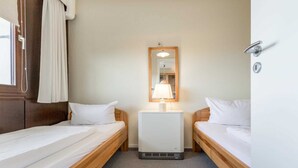 A small, clean room with two single beds, a bedside table with a lamp, a mirror, and a window with curtains. - Apartment 187 (ID 093) (Sankt Peter-Ording)