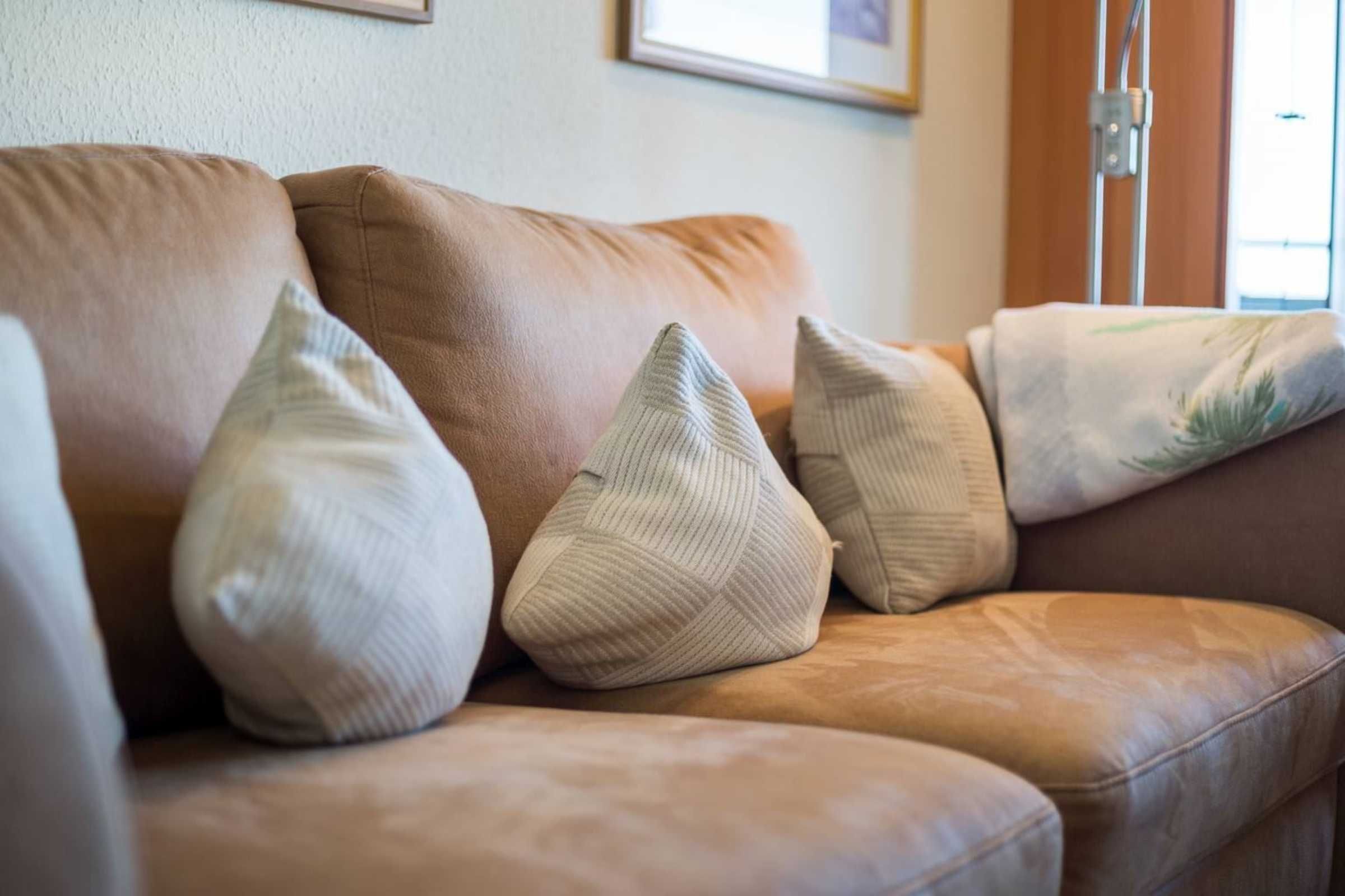 A brown leather sofa with three white pillows.