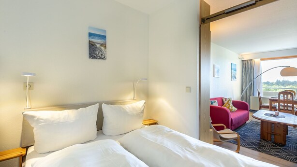 A hotel room with a bed, bedside lamps, a small table, and a view of an outdoor seating area.