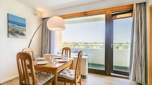 A dining area with a wooden table and chairs, a lamp, and a view of the outdoors through a large sliding glass door.