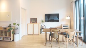 Ein modernes Wohnzimmer mit einem Holzesstisch, Stühlen, einem flachbildfernseher an der Wand und einem großen Fenster, das für natürliches Licht sorgt.