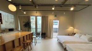 Ein Hotelzimmer mit einer Küchenzeile, einem Bett, einem Schreibtisch mit Hocker und einem Balkon mit Vorhängen.